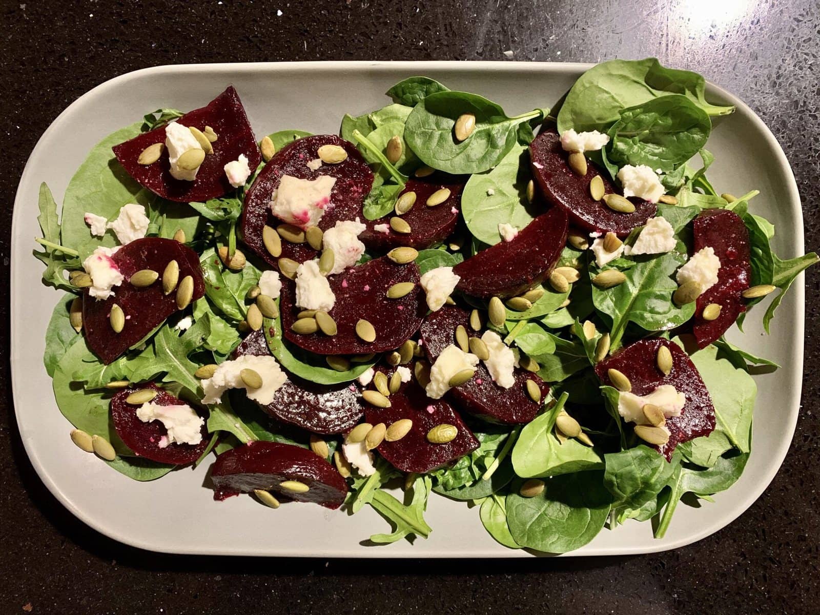 Roasted beetroot over leafy greens with crumbled cheese and pumpkin seeds
