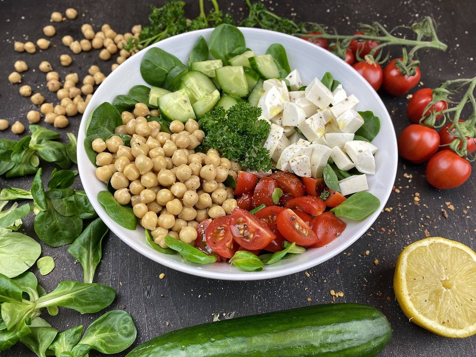 A bowl of chickpeas, cucumber, tomatoes and paneer cubes on leafy greens